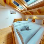 Schlafzimmer mit Doppelbett, Holzboden und Dachschrägen mit Fenstern.