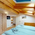 Schlafzimmer mit Holzbalkendecke, Bett, Kleiderschrank und TV. Durchgang zu weiteren Räumen.