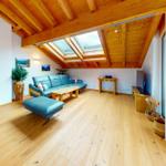 Wohnraum mit Holzboden, blauem Sofa und Dachfenstern unter Holzdecke.