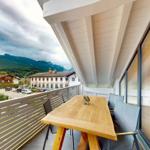 Terrasse mit Holztisch und Stühlen. Blick auf Berge und Gebäude.