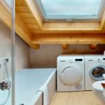 Badezimmer mit Badewanne, Waschmaschine und Trockner unter Holzdecke mit Dachfenster.