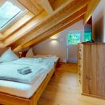 Schlafzimmer mit Doppelbett, kleinem Bett und Dachschrägen. Holzdecke und Fenster.
