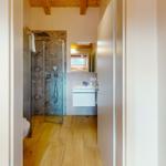 Badezimmer mit Dusche, Waschbecken und Toilette. Holzfußboden und Holzbalken an der Decke.
