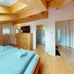 Schlafzimmer mit Holzboden, Dachschrägen und TV. Blick in Bad und angrenzenden Raum.