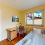 Ein Schlafzimmer mit Doppelbett, Schreibtisch und Fenster mit Blick auf Holzhaus.