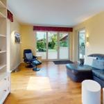 Wohnzimmer mit Ledersofa, Sessel, Bücherregal und Blick auf den Garten.
