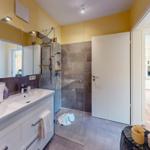 Badezimmer mit Dusche, Waschbecken und Spiegelschrank. Tür führt in Wohnbereich.
