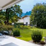 Terrasse mit Liegestühlen, Garten mit Rasen und Bäumen, Bergpanorama im Hintergrund.