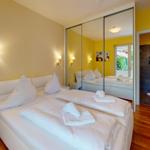 Schlafzimmer mit weißem Bett, Spiegelschrank und angrenzender Dusche.