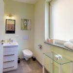 Badezimmer mit Dusche, Waschbecken und Toilette. Fenster mit Handtüchern.