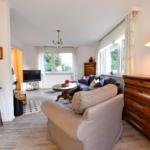Wohnzimmer mit Sofa, Couch, TV und Holzmöbeln. Fenster mit Blick auf Garten.