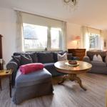 Wohnzimmer mit Sofa, Sessel und Holztisch. Fenster und Tür zur Außenterrasse.