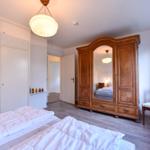 Zwei Betten, ein Holzschrank mit Spiegel und eine Stuhl am Fenster.