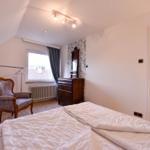 Schlafzimmer mit Doppelbett, Stuhl, Schrank und Fenster mit Blick auf Dach.
