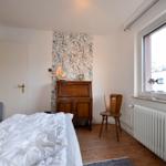Schlafzimmer mit Bett, Holzfußboden, Schrank und Fenster mit Blick auf Gebäude.