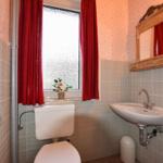 Badezimmer mit Toilette, Waschbecken und Fenster mit roten Vorhängen.