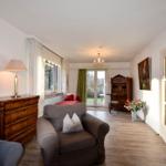 Wohnzimmer mit Sessel, Schrank und Türen zum Garten.