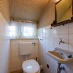 Badezimmer mit Toilette, Waschbecken und Fenster mit Vorhängen.