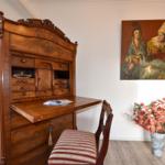 Antikschreibtisch mit Stuhl, Wandbild und Blumenarrangement im Raum.