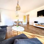 Wohnzimmer mit Sofa, Esstisch und Fernseher an der Wand.