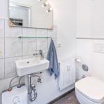 Badezimmer mit Waschbecken, Spiegel, Toilette und Heizkörper.