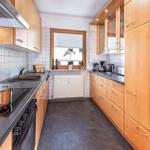 Küche mit Holzschränken, Edelstahlspüle und Fenster mit Pflanze.