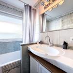 Bad mit Waschbecken, Spiegel und Badewanne mit Fenster.