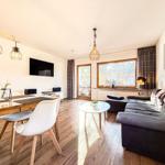 Wohn- und Essbereich mit Sofa, Tisch und TV. Holzfußboden und große Fenster.