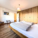 Schlafzimmer mit Doppelbett, Holzwand und Sessel. Auf dem Bett liegen Handtücher.