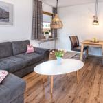 Wohn- und Essbereich mit Sofa, Tisch und Stühlen. Holzboden und Wandbild mit Bergmotiv.