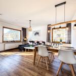 Wohn- und Essbereich mit Holzboden, Sofa, Esstisch und Fenstern.