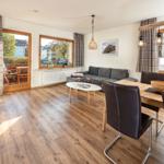 Wohn- und Essbereich mit Holzboden, Sofa, Esstisch und Blick auf Balkon.