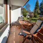 Terrasse mit Holztisch, zwei Stühlen und Blick auf grünen Garten.