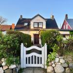 Haus mit weißem Tor und grünen Hecken im Vordergrund.