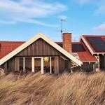 Holzhaus mit rotem Dach und Solarpanelen im Hintergrund. Vorne hohes Gras.