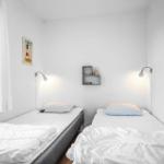 Zwei Einzelbetten mit weißen Laken und Wandlampen in einem hellen Raum.