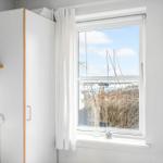 Ein Fenster mit Blick auf einen Hafen. Weiße Vorhänge und ein Schrank sind sichtbar.