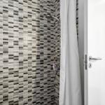 Dusche mit Mosaikfliesen und Duschvorhang. Tür und Wand mit Haken sichtbar.