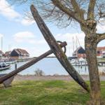 Großer Holzanker vor einem Hafen mit Booten und Häusern.