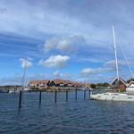 Segelyacht liegt im Hafen vor modernen Häusern mit roten Dächern.