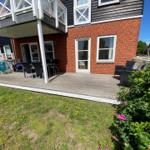 Haus mit Terrasse, Garten und Gartenmöbeln unter blauem Himmel.