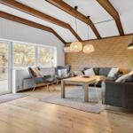 Wohnzimmer mit Holzboden, Sofa, Sessel und Fenster zur Außenseite.