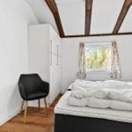 Schlafzimmer mit Bett, Stuhl und Fenster mit Vorhängen.