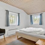 Schlafzimmer mit Bett, Stuhl und zwei Fenstern mit Vorhängen.