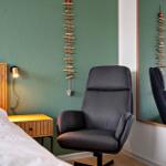 Schlafzimmer mit Bett, Nachttisch und Sessel. Wanddekoration und Spiegel sichtbar.