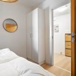 Schlafzimmer mit weißem Bett, Kleiderschrank und runden Spiegel. Durchgang zu angrenzender Raum.