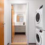 Waschraum mit Waschmaschine und Trockner. Blick in das Badezimmer mit Spiegel und Waschbecken.