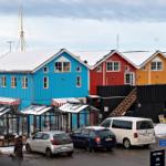 Farbige Häuser am Hafen mit Schnee auf Dächern und geparkten Autos.