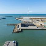 Hafen mit Windrad, Boot und Industriegebäuden an der Küste.