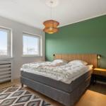 Schlafzimmer mit Bett, grüner Wand und zwei Fenstern.